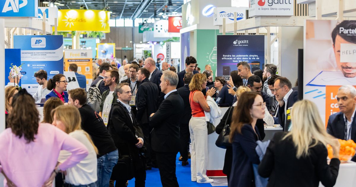 Scène animée dans les allées d'un salon professionnel avec de nombreux visiteurs et exposants discutant autour des stands, représentant une ambiance dynamique et conviviale.
