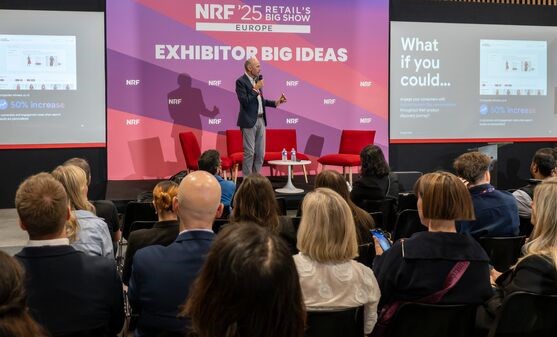 Man holding a microphone in front of a screen with the words Exhibitor Big Ideas