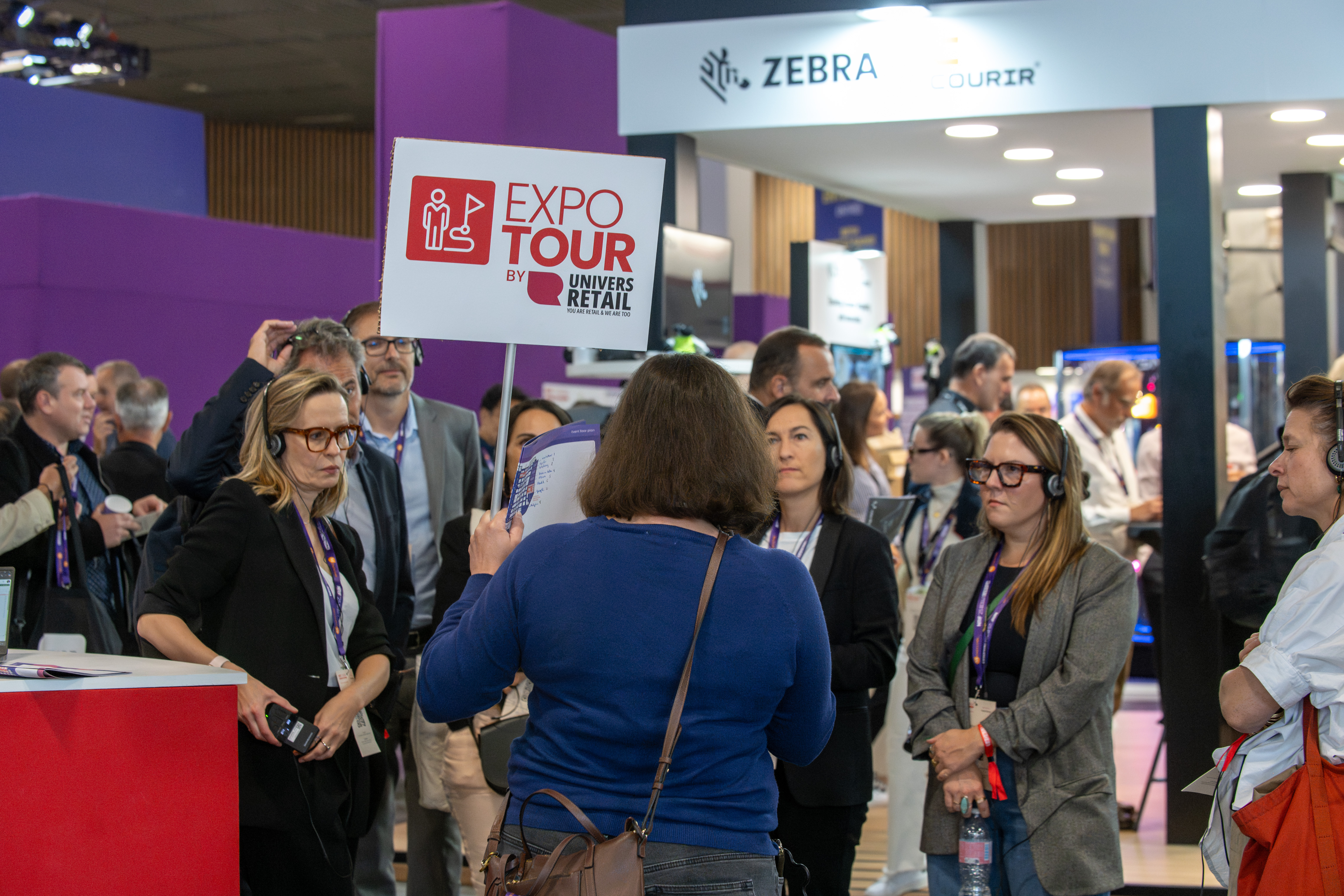 View of the NRF exhibition floor with a crowd of attendees gathered in front of a large "EXPO Tour" banner featuring the Univers Retail logo.
