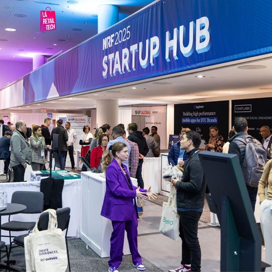 Vue du Startup Hub lors du NRF 2025, avec des visiteurs échangeant devant les stands d'exposants et un grand panneau indiquant NRF 2025 Startup Hub.