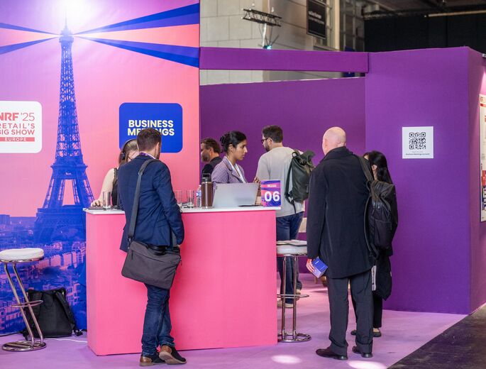 Attendees networking at the Business Meetings area of NRF 2025: Retail’s Big Show Europe, in front of a pink Eiffel Tower backdrop.