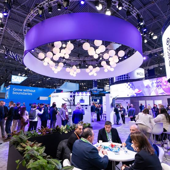 Vue du salon NRF 2025 avec des visiteurs réunis autour des stands SAP et KPCYNYX sous une grande structure lumineuse suspendue.