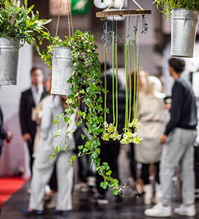 Hanging plant decorations with blurred visitors in the background at a professional trade show.