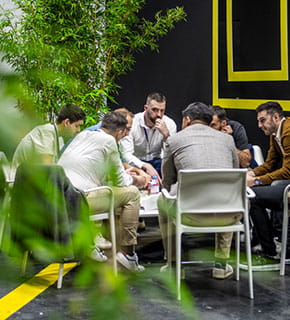 Group of men seated around a table in a discussion area during the show.