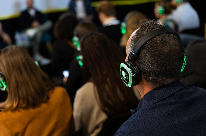 Participants équipés de casques audio lors d'une conférence illustrant une expérience immersive et interactive.