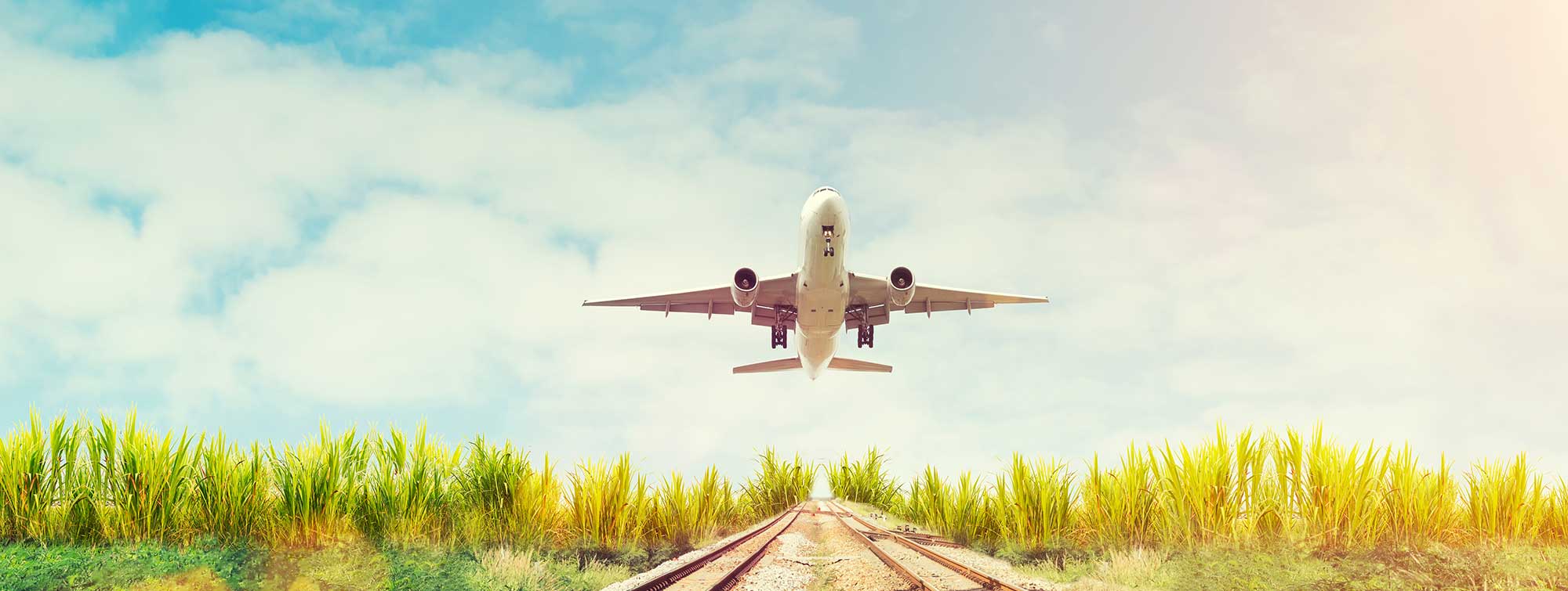 Airplane taking off above tracks and a green meadow under a clear sky.