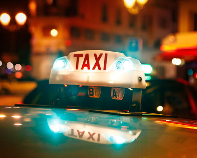 Enseigne lumineuse de taxi à Paris de nuit avec reflets sur le toit de la voiture.