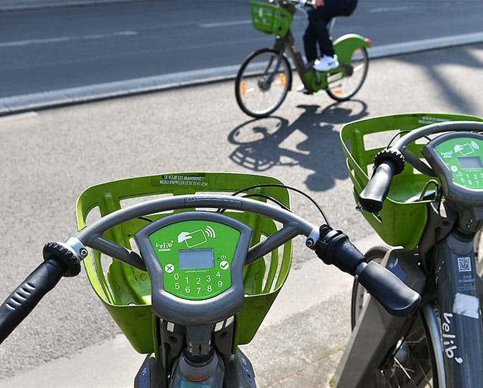 Vélib' en station à Paris, avec un cycliste en arrière-plan roulant sur un vélo similaire.